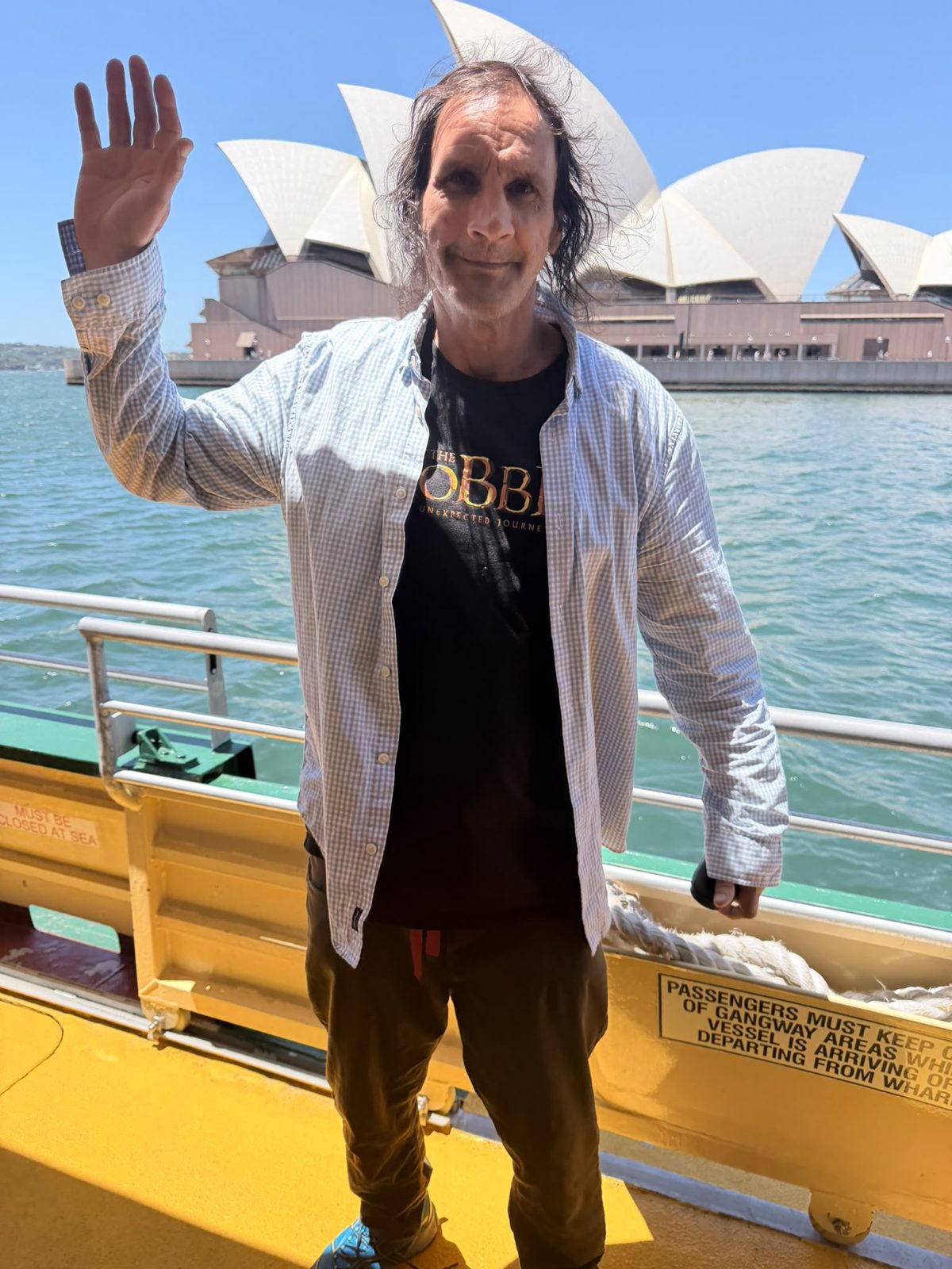 An NDIS participant waving in front of the Sydney Opera House on a harbour ferry outing