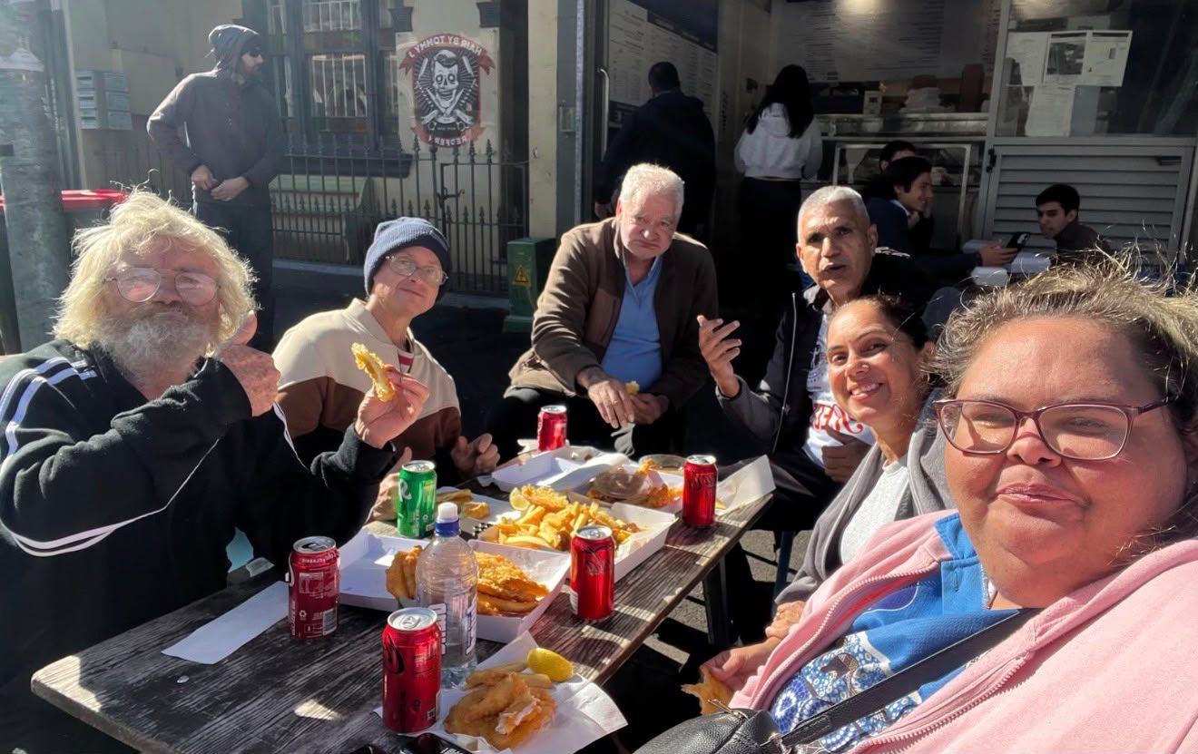 Tegrity participants and support workers sharing a meal together on a sunny community outing